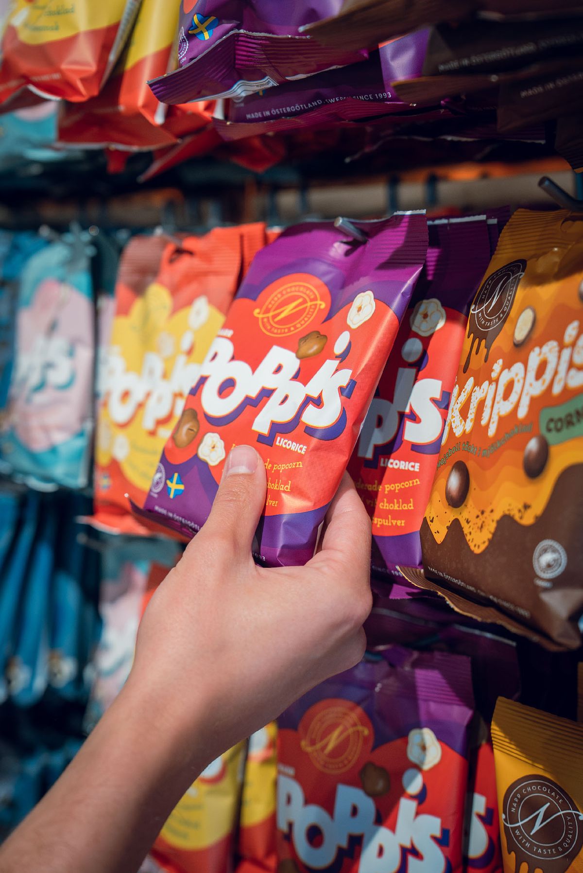 Hand som plockar en påse Pop's chokladdragerade popcorn från butikshyllan.