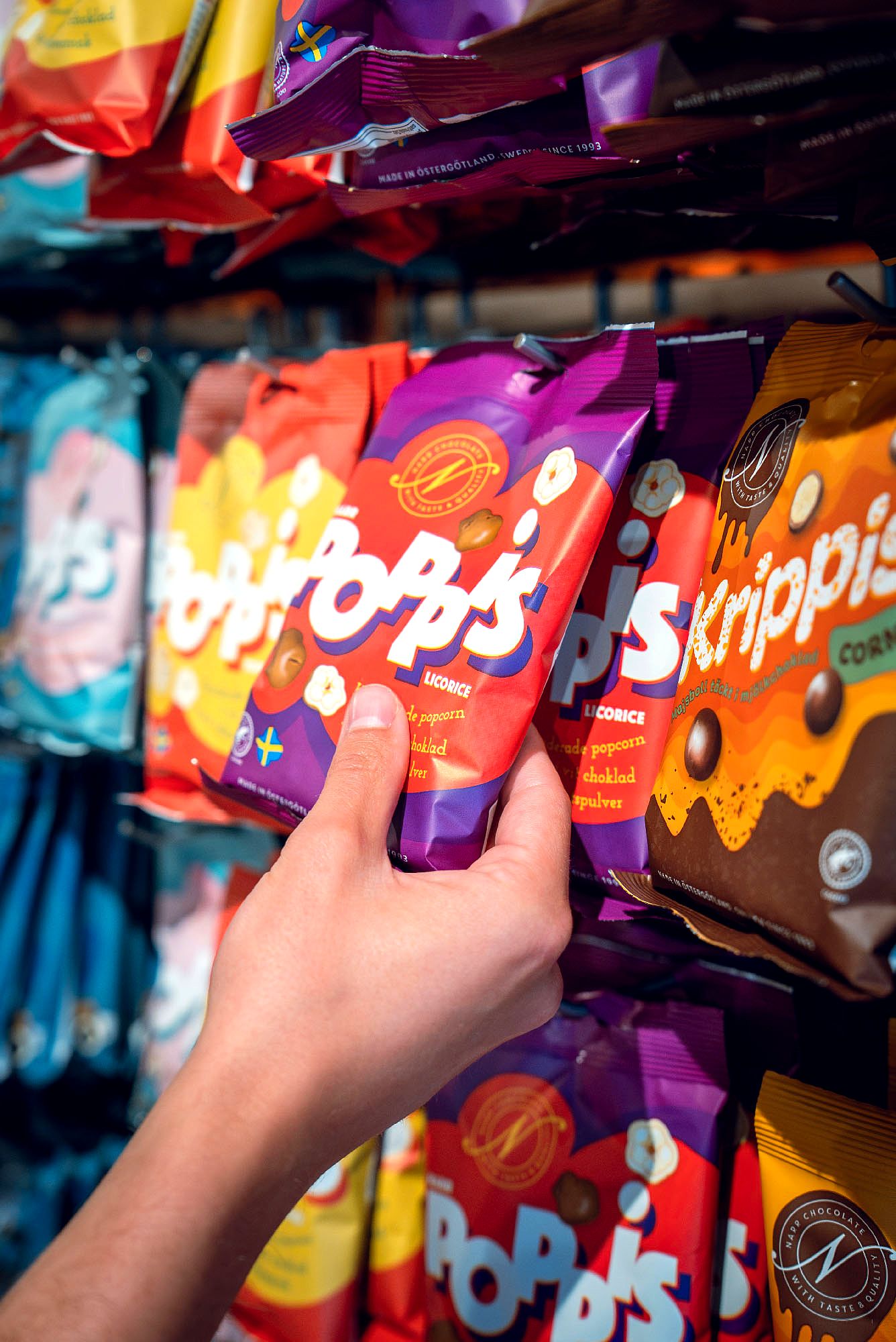 Hand som plockar en påse Pop's chokladdragerade popcorn från butikshyllan.