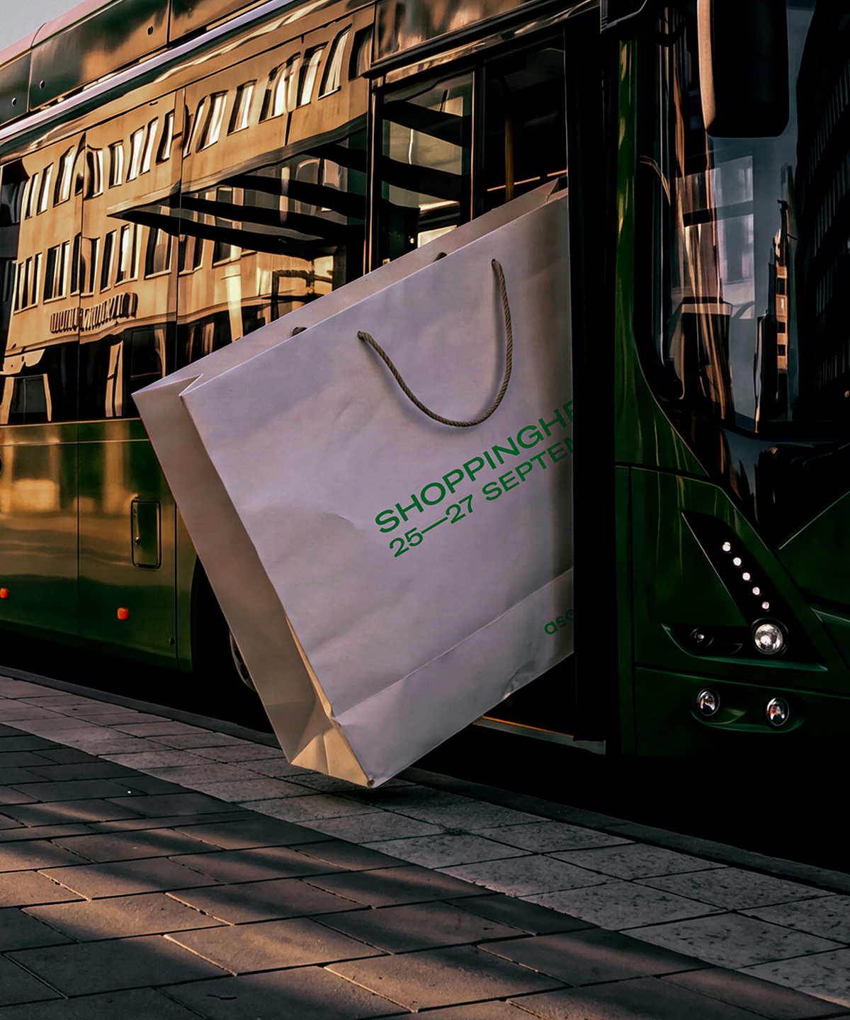 Massiv vit shoppingpåse med texten "Shoppinghelg 25—27 September" som fastnat i dörrarna på en grön stadsbuss